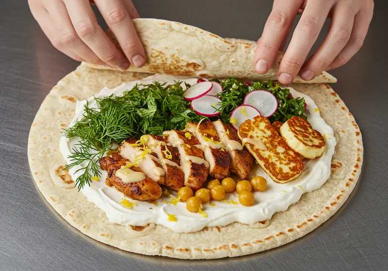 Assembling shawarma wrap with labneh, chicken, herbs, and toppings
