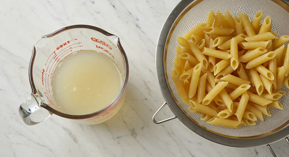 Reserved pasta water in cup next to drained pasta