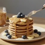 Fluffy banana egg pancake stack drizzled with almond butter on ceramic plate