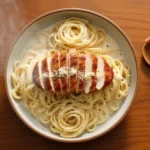 A steamy bowl of creamy Chicken Alfredo pasta with seasoned chicken, perfectly plated on a dark wood table.
