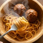 30-Minute Magic: Easiest Spaghetti and Meatballs for Happy Kids A complete serving of easy spaghetti and meatballs for kids in a wooden bowl, with steam rising and a hand holding a fork.