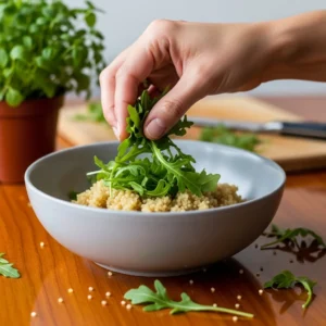 A hand adding quinoa and arugula to a ceramic bowl as the base for the salmon bowl.