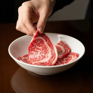 A hand placing thin slices of ribeye steak into a white ceramic bowl for the Beef Bulgogi marinade.