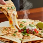 How To Cook Easy Chicken Quesadilla in 30 Minutes (Kid Approved) A hand holding a slice of chicken quesadilla with a long, stretchy cheese pull on a dark wood table.