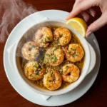 A completed bowl of sizzling garlic butter shrimp with steam rising, garnished with lemon on a dark wood table.