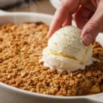A baked apple crisp with a steaming, golden oat and pecan topping, served with melting vanilla ice cream.