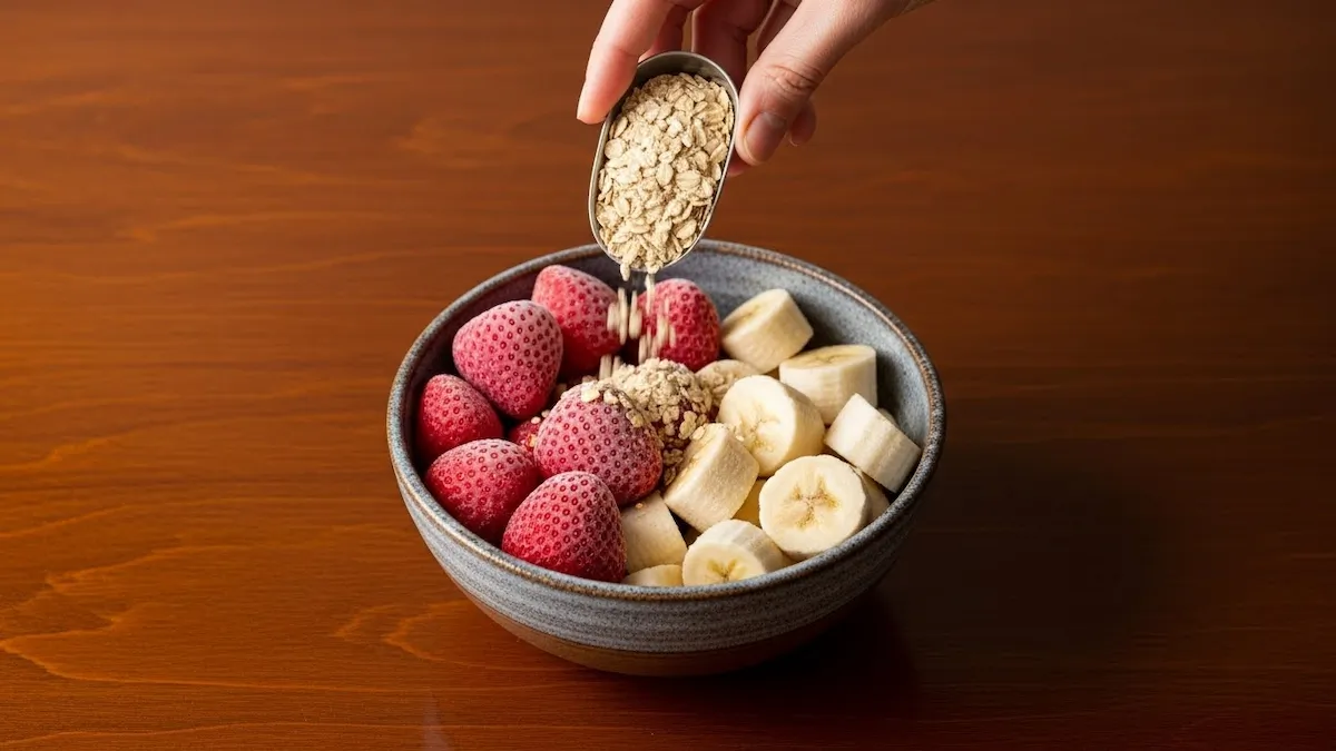 Ingredients for a strawberry banana smoothie in a ceramic bowl, including frozen fruit, oats, and yogurt.