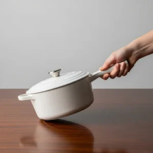 A light-colored ceramic Dutch oven or soup pot with a handle, held by a hand.
