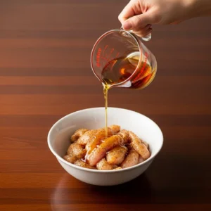 Pouring a lime and maple syrup glaze over seasoned chicken in a bowl.