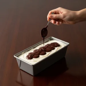 A hand drizzling glossy, melted dark chocolate over the white creamy protein bar layer.