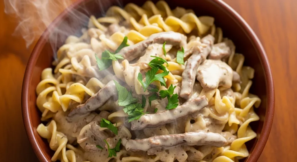 Close-up overhead view of a rustic ceramic bowl filled with creamy beef stroganoff, showing tender beef strips and mushrooms coated in thick sauce, garnished with fresh parsley, with light steam rising.