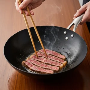 A human hand using wooden chopsticks to sear slices of beef in a hot wok with a golden-brown crust forming.
