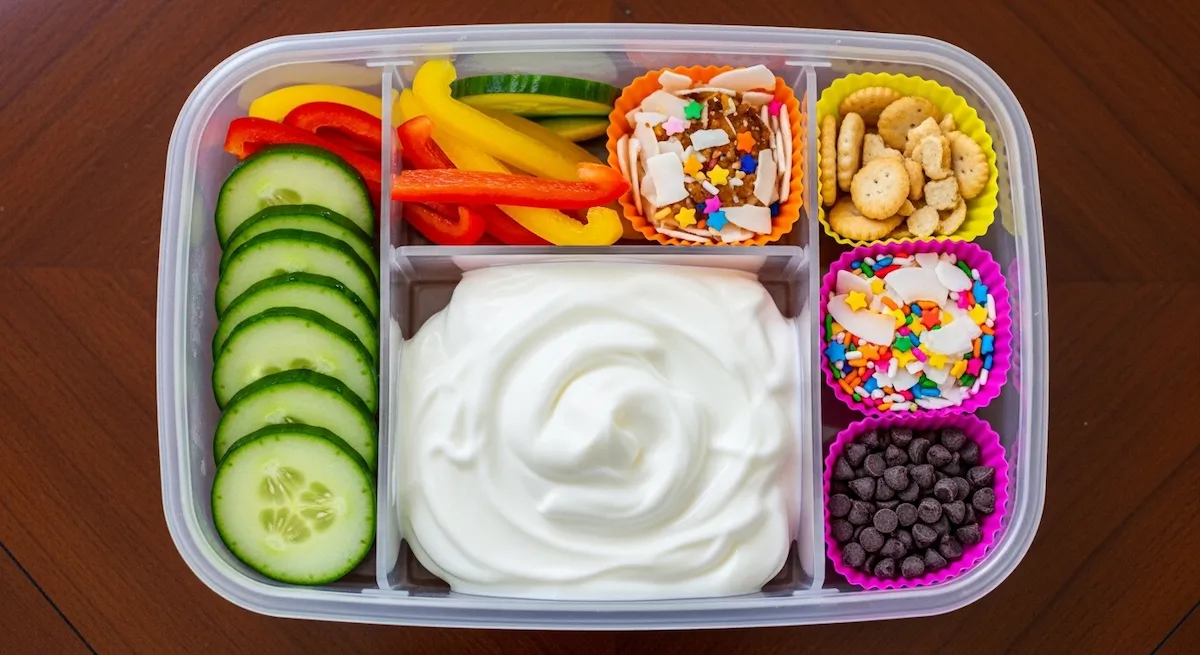 Complete Greek yogurt protein box lunch box for picky kids with cucumber bell peppers crackers coconut sprinkles chocolate chips